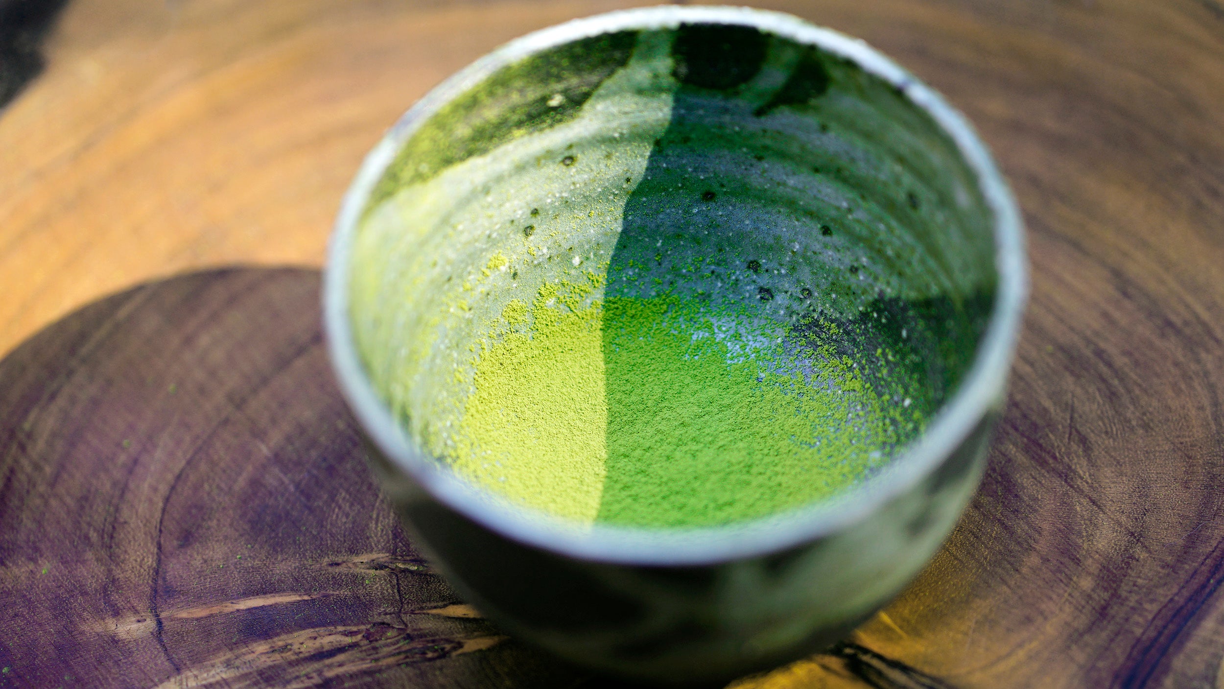 Bright green matcha powder in a matcha bowl on top on a piece of wood