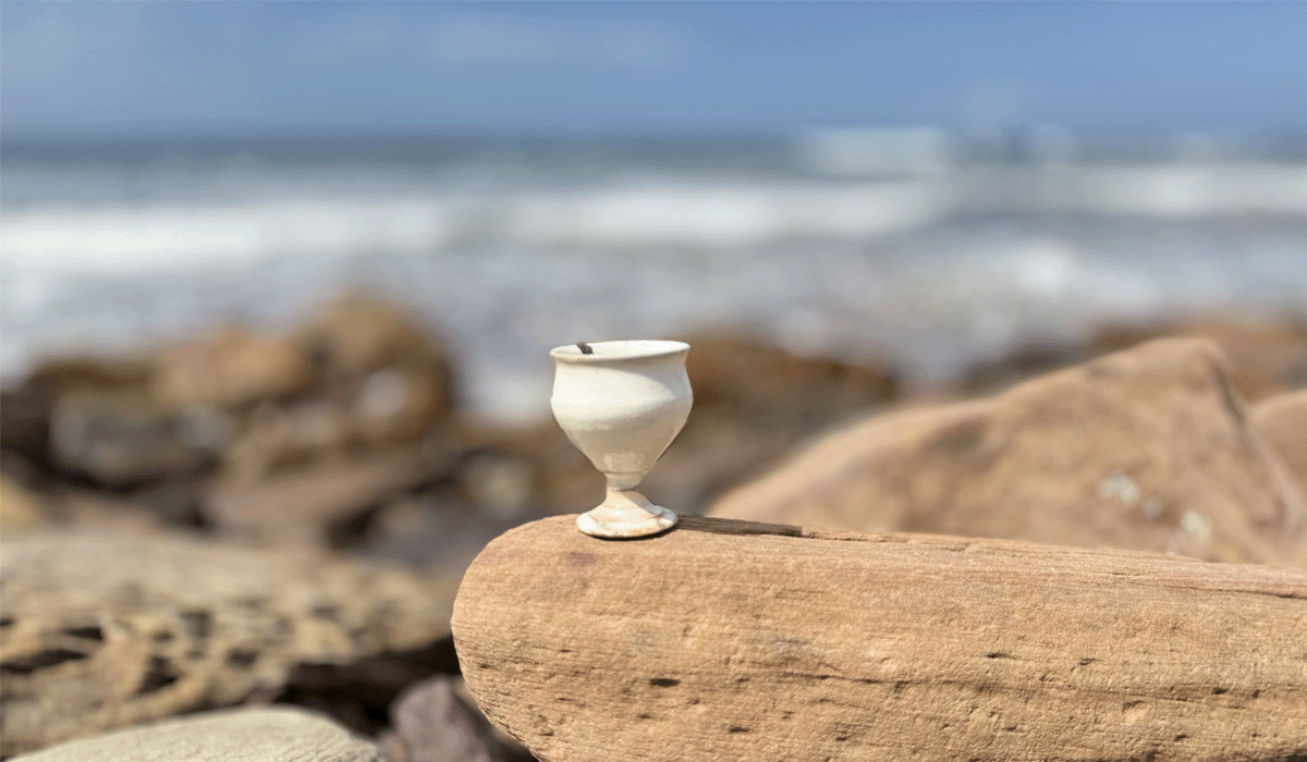 White ceramic cup on a rock with ocean in the background