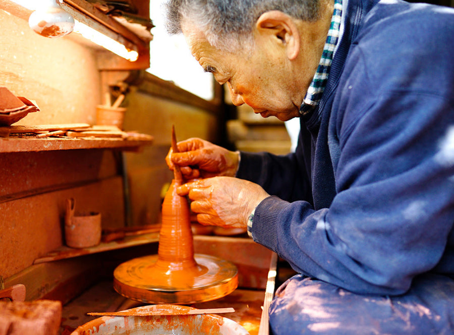 Artist making teapots on a pottery wheel in a workshop.
