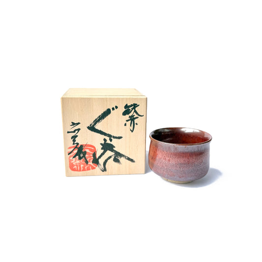 handcrafted AKAAKA ceramic Yunomi teacup with a deep crimson and smokey grey glaze, alongside a traditional wooden box with Japanese characters written in black.