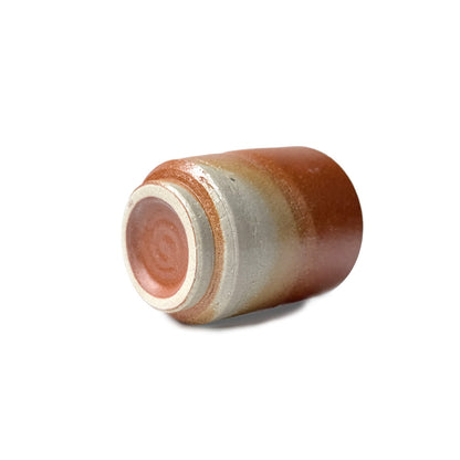 The bottom of a cylindrical ceramic teacup with a gradient color from brown to beige on a white background